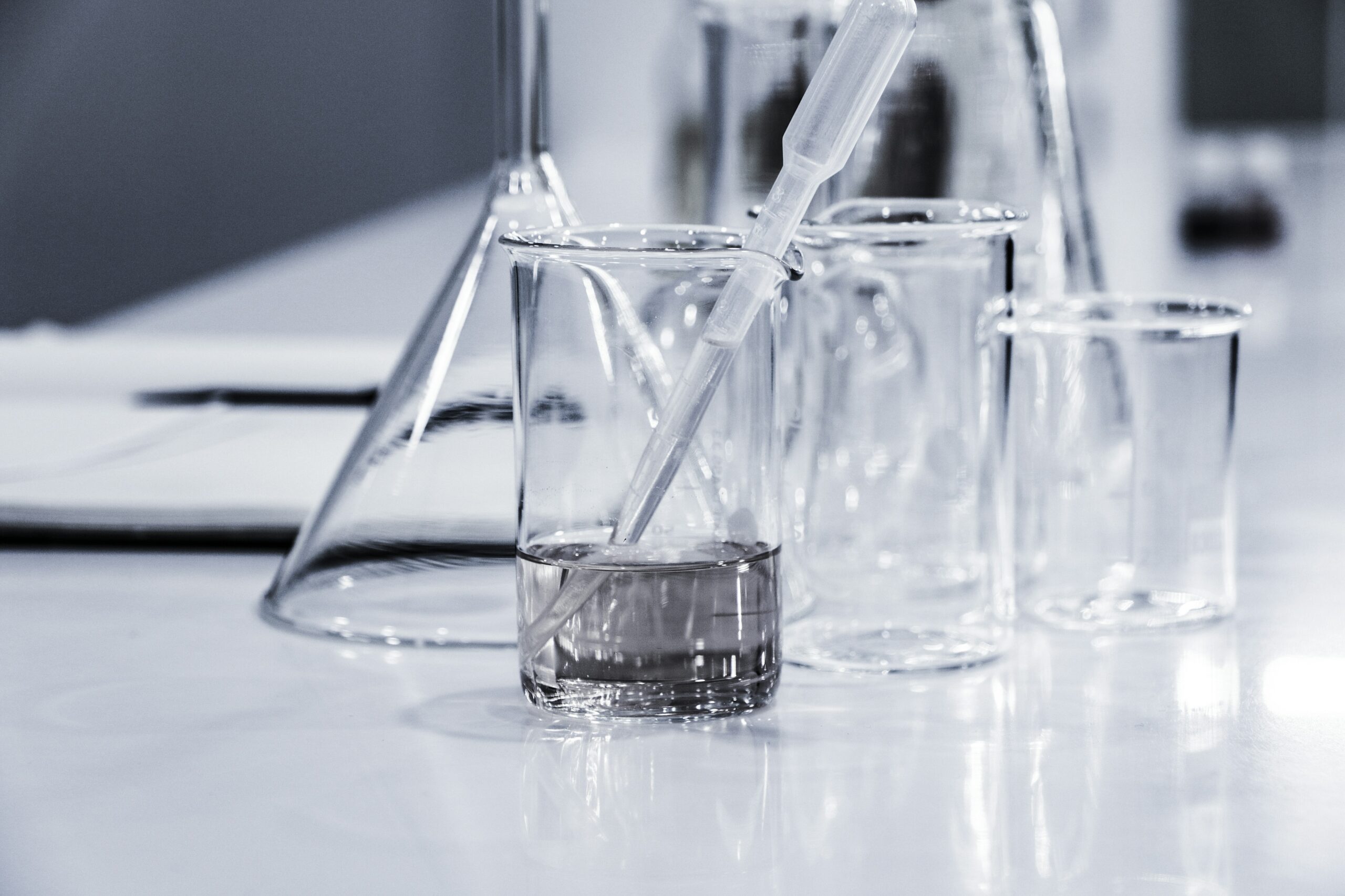 Laboratory glassware including beakers, flask, and dropper with clear liquid for water quality testing - whole house water filter maintenance equipment